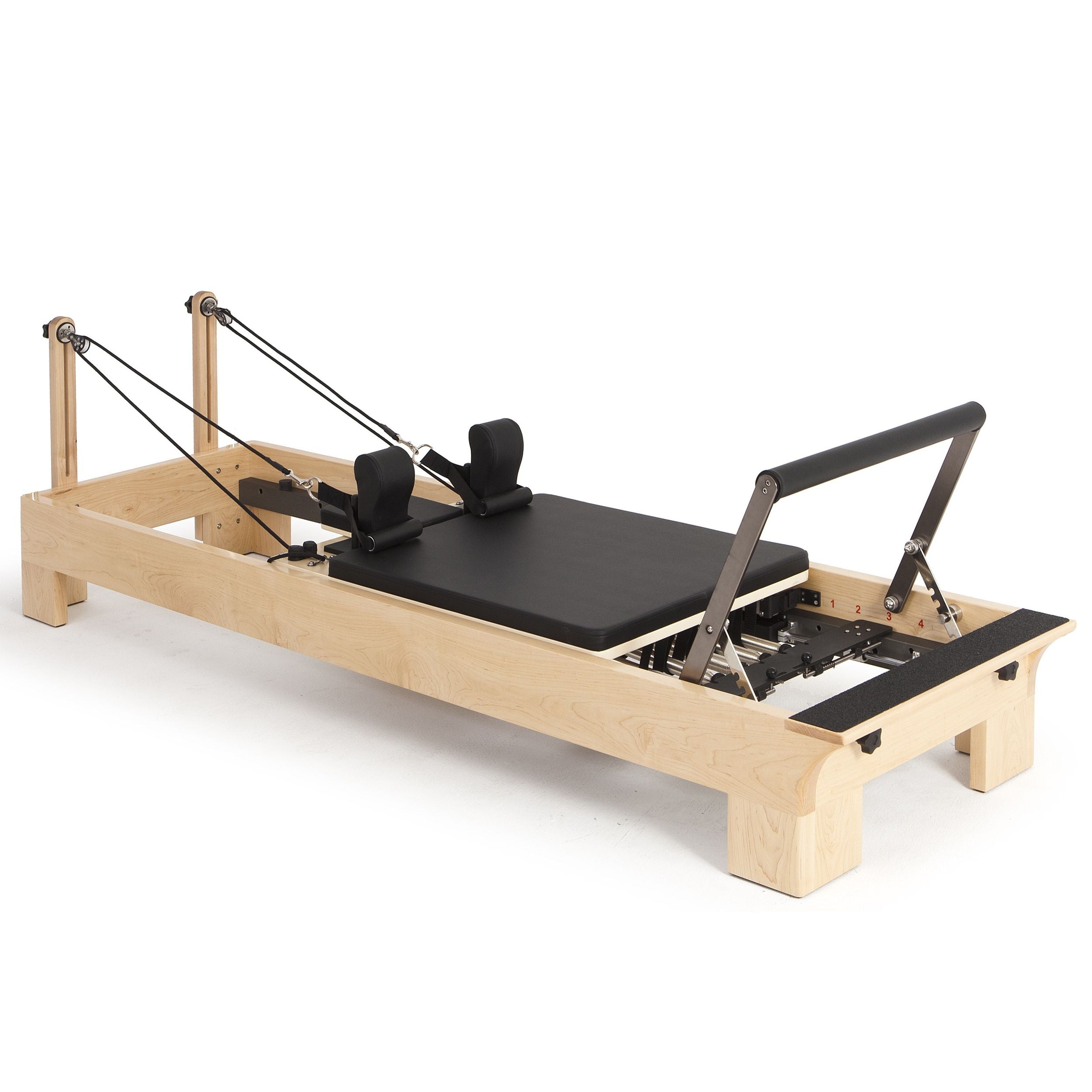 Pilates reformer with wooden frame and black cushion on a white background