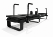 Side angle view of the Elina Pilates Corextreme black reformer showing the full frame, handles, carriage, and platform